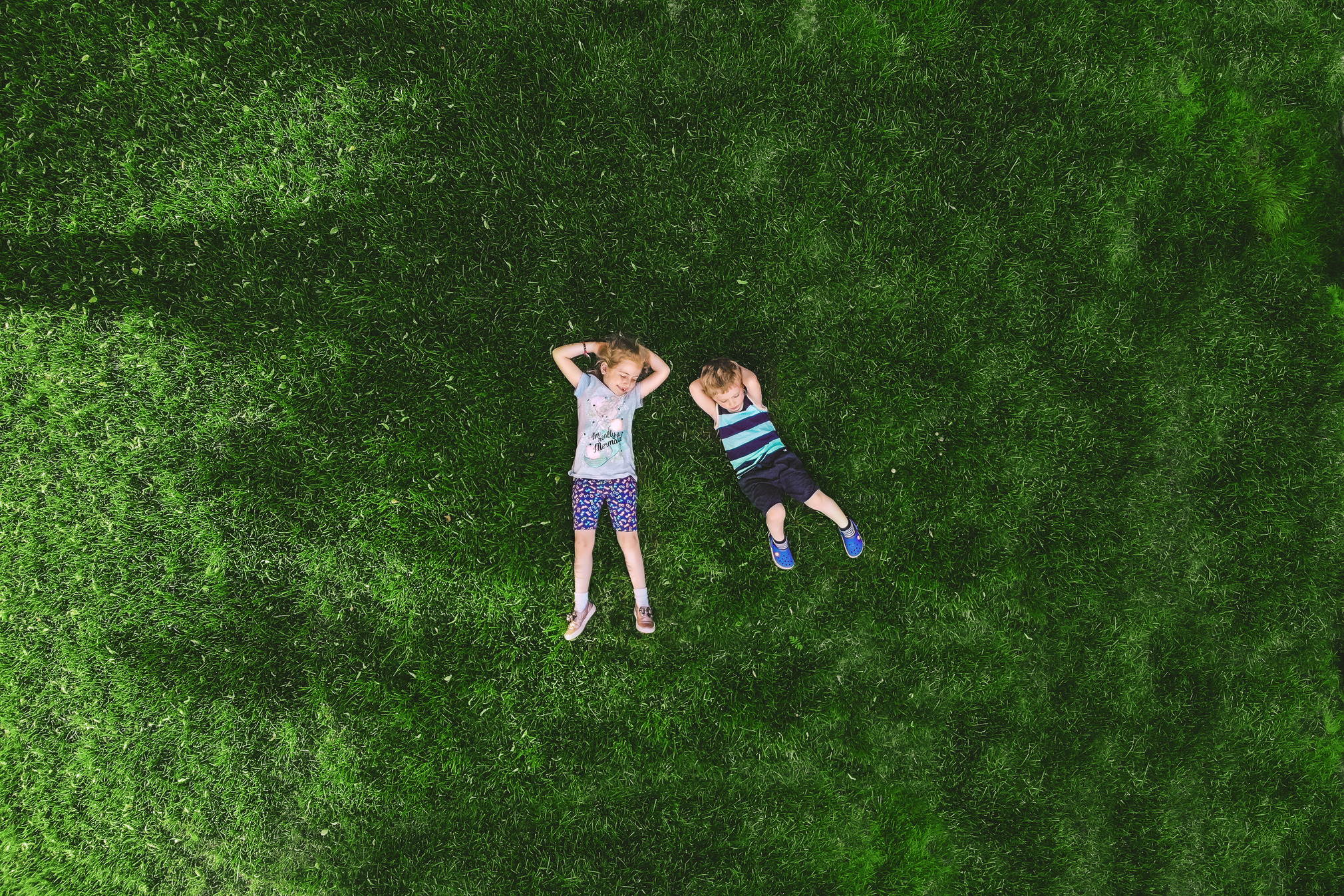 Two kids lying on a grassy field, aerial view