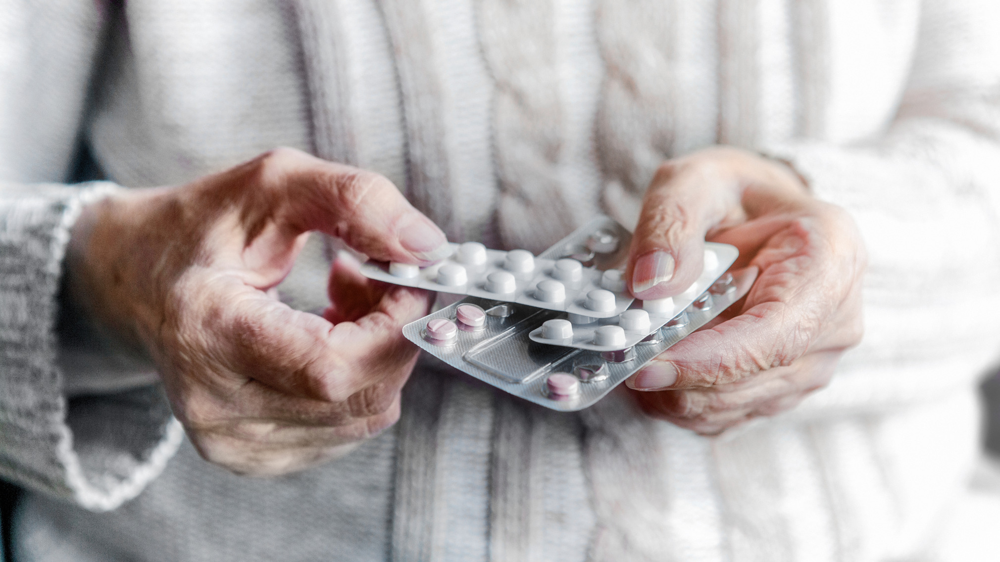 Close-up of a person’s hands holding two blister packs of tablets, with several white and pink pills visible.