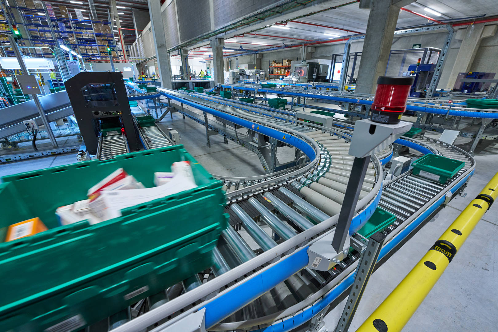 In a Cencora shipping facility, a green plastic bin holding boxes of medication moves through a shipping line.