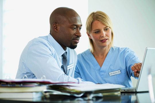 Businessman and healthcare worker discussing data showcased on laptop