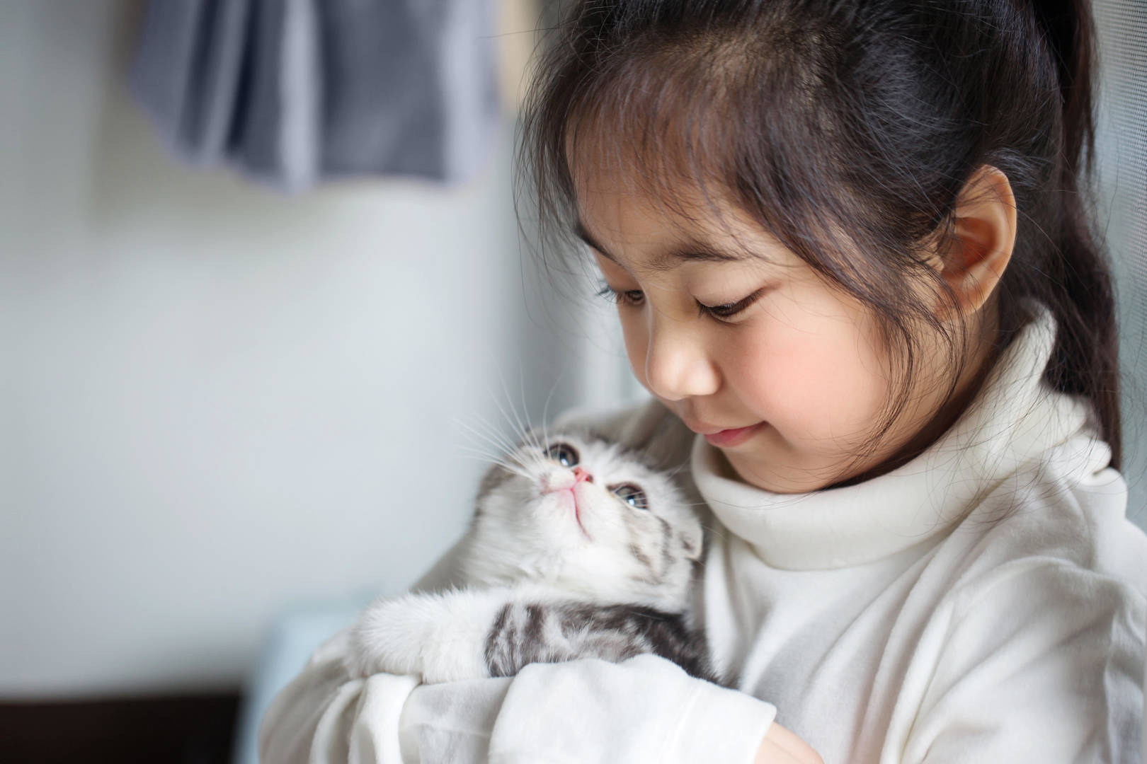Une jeune fille, les yeux baissés, sourit à un chaton qu’elle tient dans ses bras.