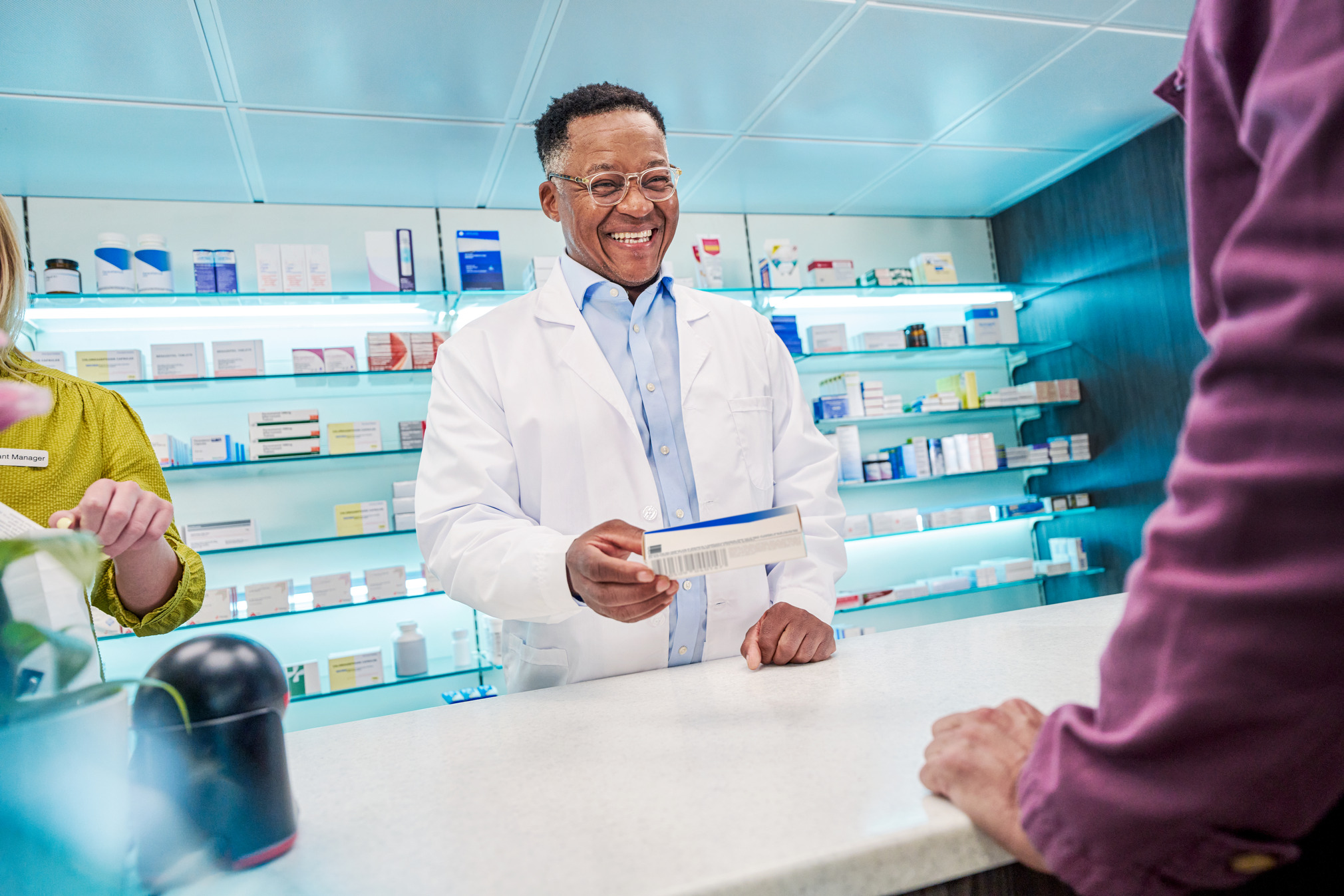 Smiling pharmacist behind the counter handing the medication to the customer.