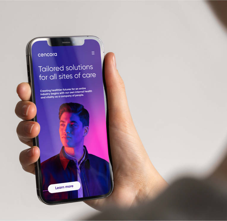 Une main tient un téléphone portable et le nouveau site web de Cencora s’affiche sur l’écran du navigateur.
