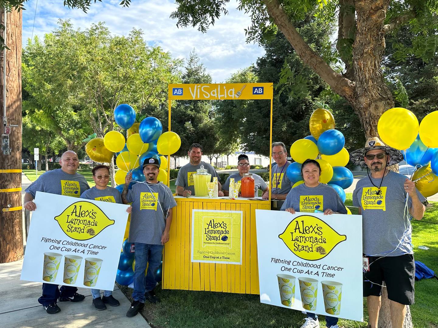 Huit bénévoles de Cencora posent devant un stand de limonade jaune avec des affiches et des t-shirts sur lesquels on peut lire « Alex's Lemonade Stand ».