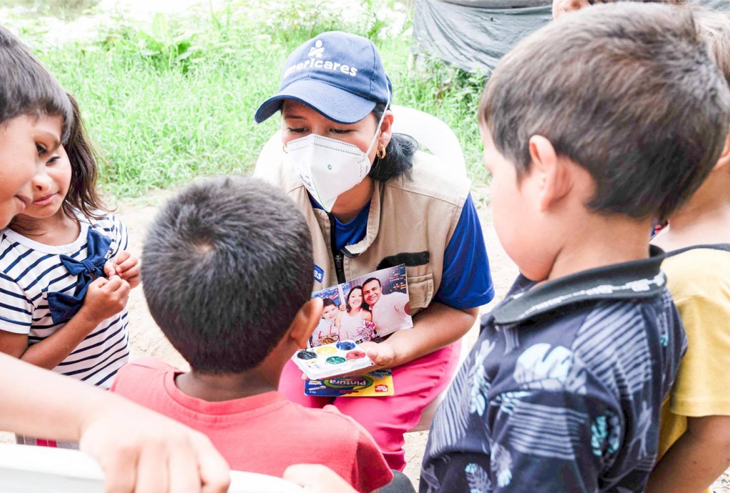 A woman wearing a cap and face mask is interacting with a group of five children.
