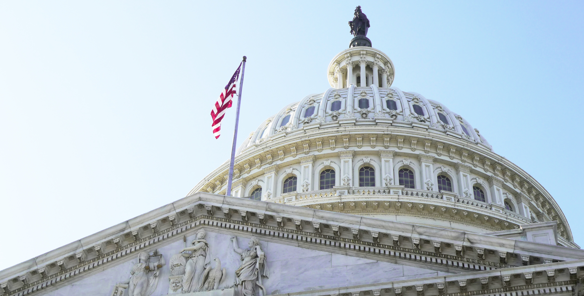 A picture of the top of government building set against a blue sky. The flag of the United States flies on a pole from the roof.