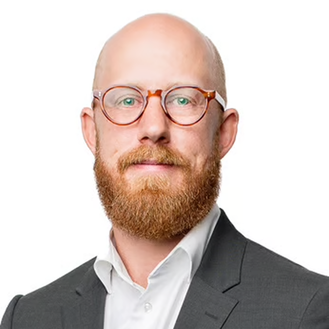 A headshot of a Product Manager at Cencora, a middle aged man with a medium length beard, round red prescription glasses, and a slight smile, dressed in a gray suit conveying leadership and professionalism.