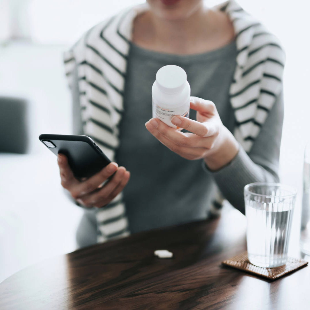 Woman reviewing information about medication on her phone while holding the medicine in her hand