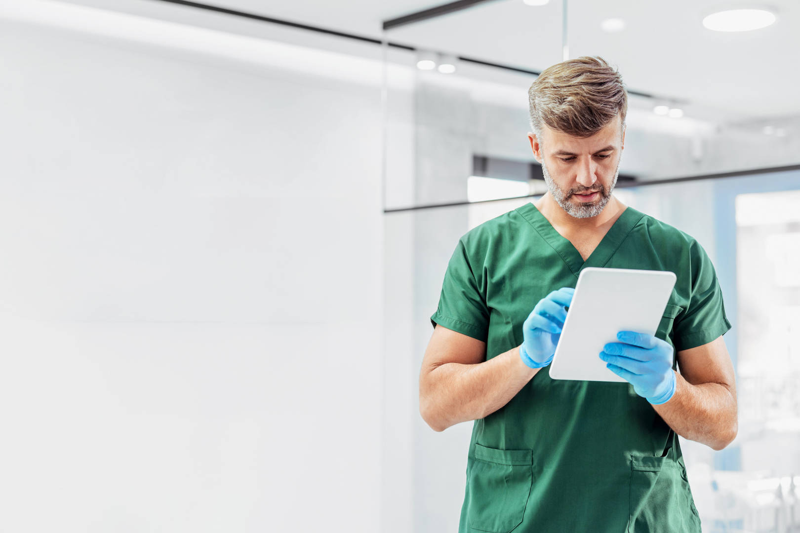 Healthcare professional in green scrubs using a tablet in a hospital