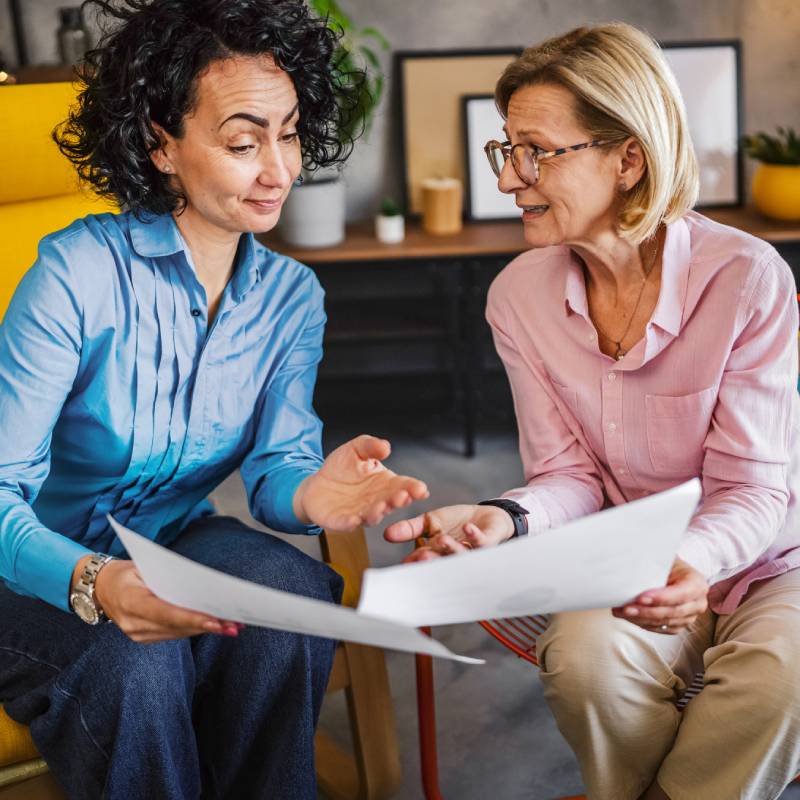 Two businesswomen discussing and comparing two documents in a casual meeting area
