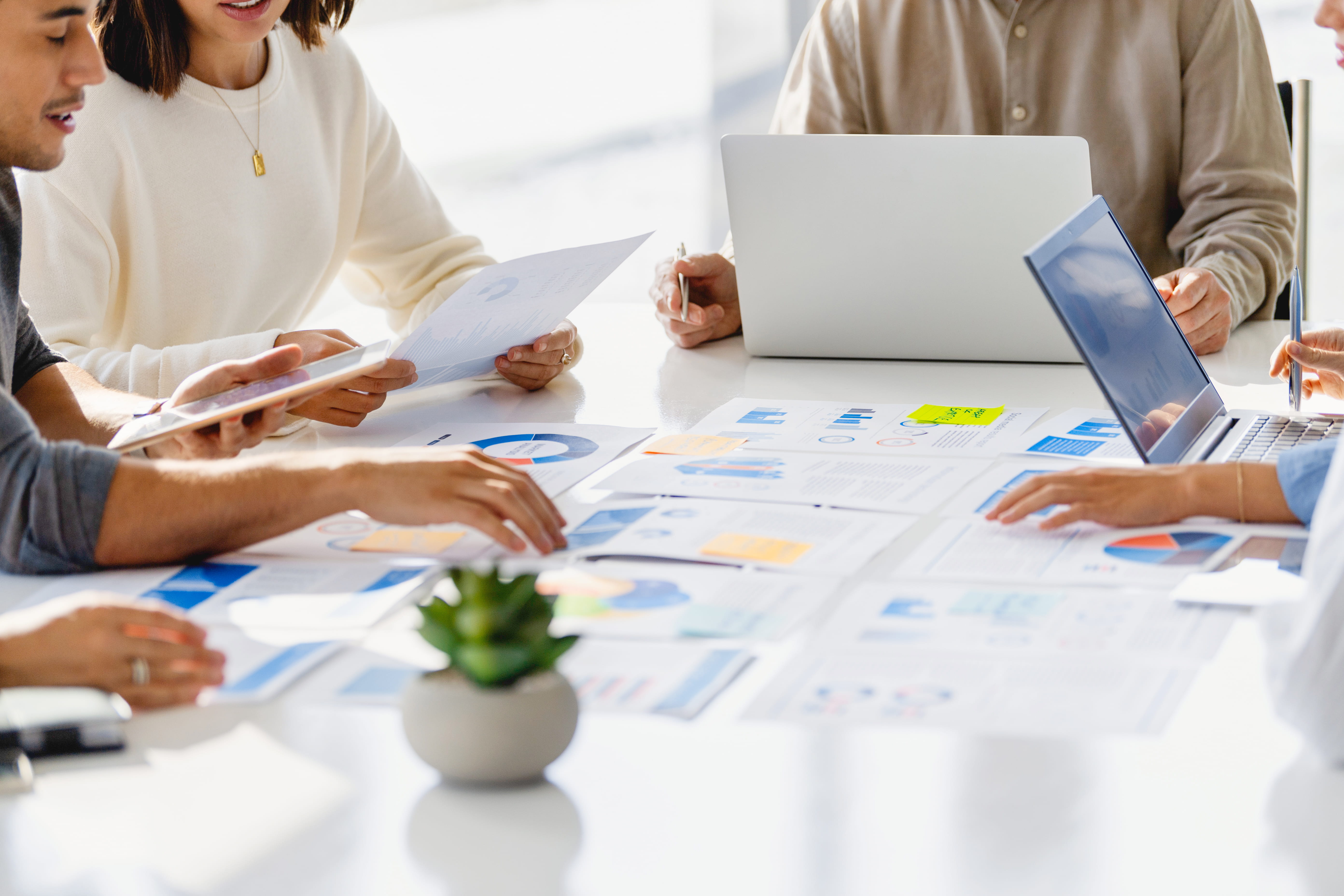 Group of team members collaborating together on a work table with laptops and paperwork showcasing statistics and marketing data. 