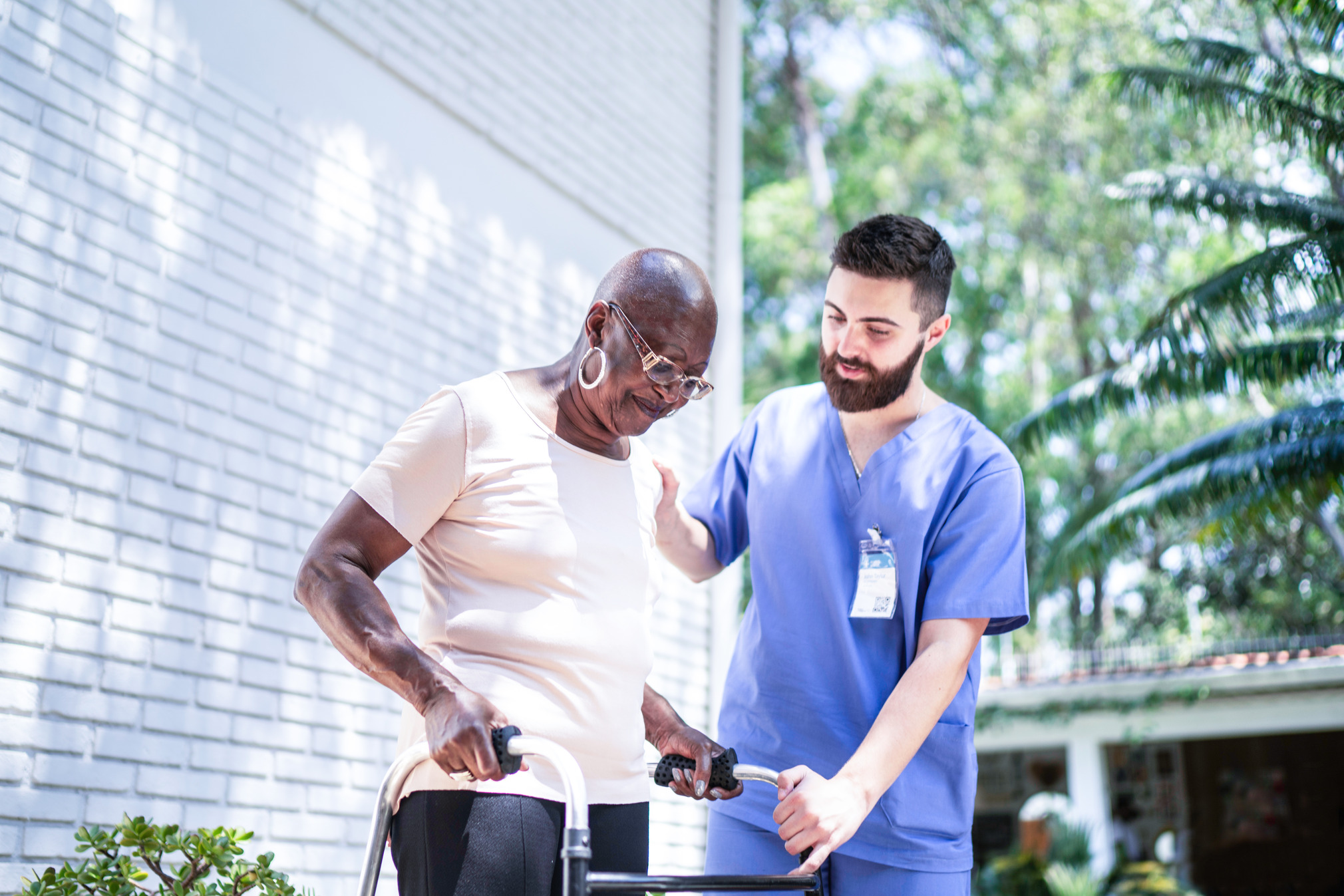 Young male nurse helps an elder woman to walk in a hospice.