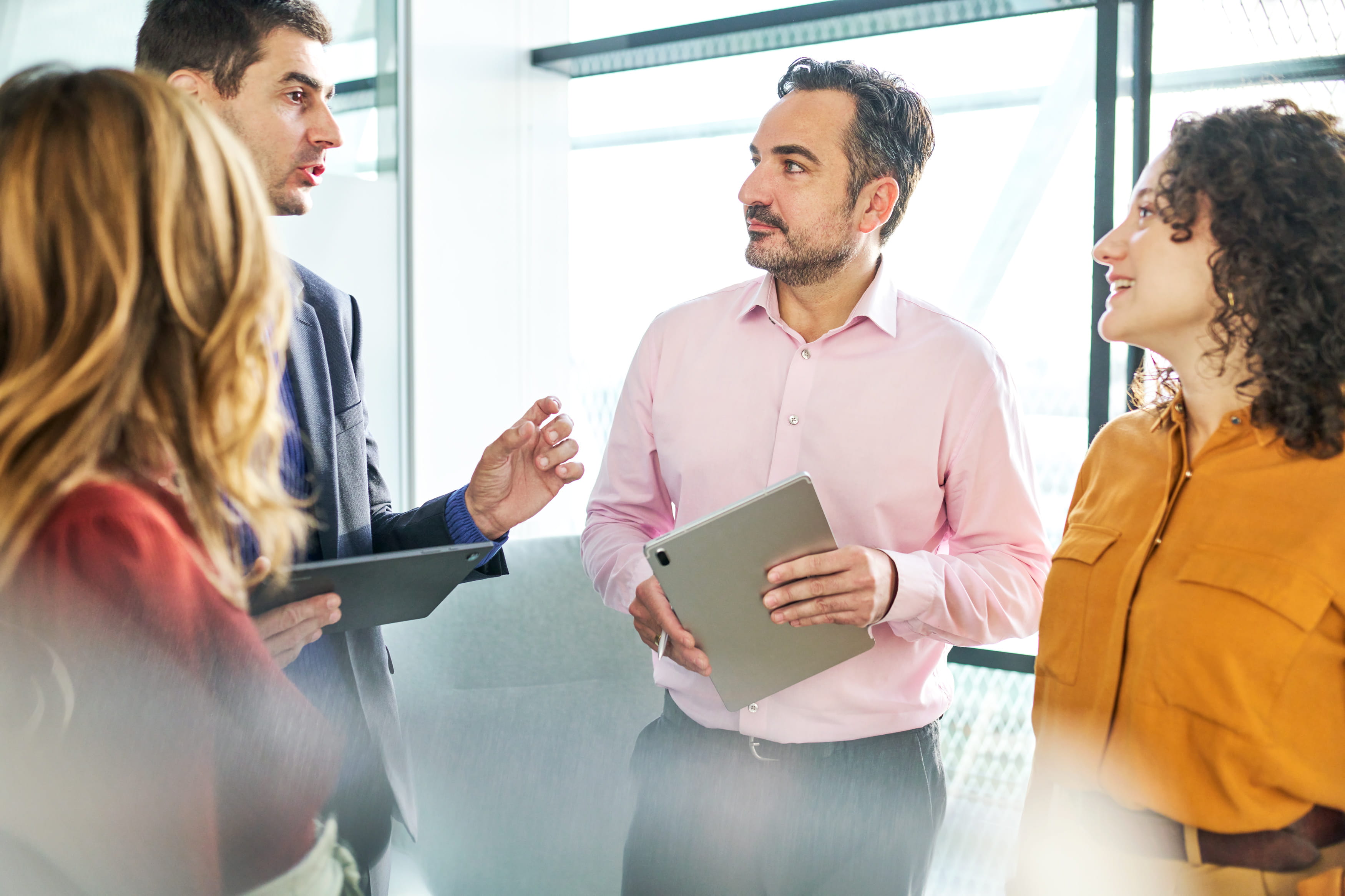 a group of employees in a standup discussing a project together while smiling and listening attentively to someone speaking in the group. 