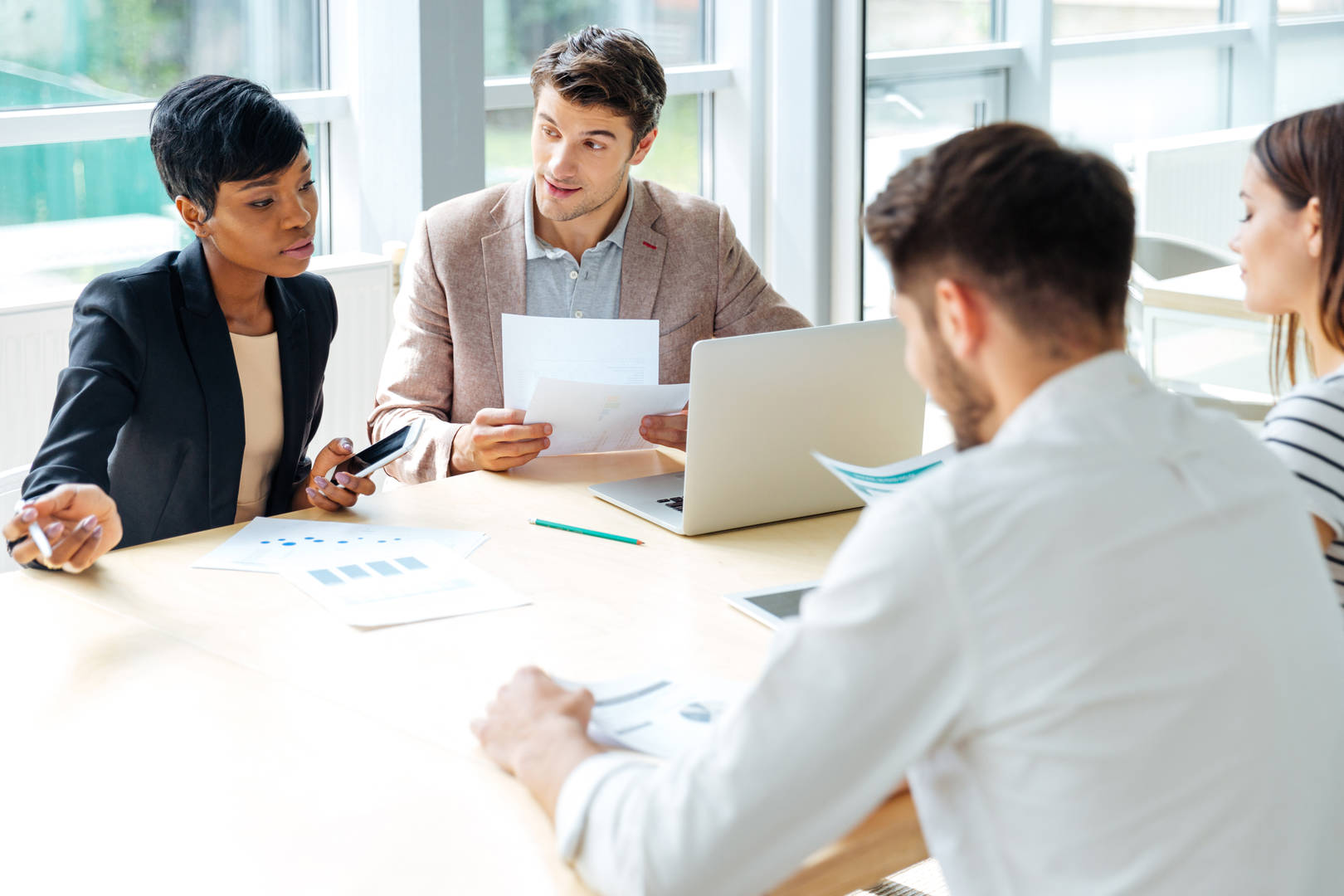 A group of employees working together on a conference table with documents and laptops discussing their findings. 