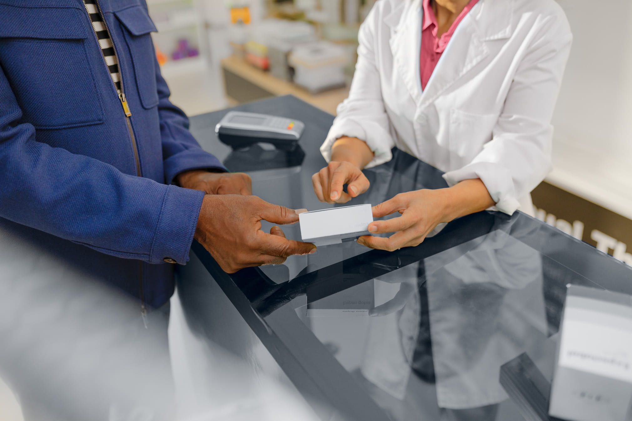 Close-up of a female pharmacy employee handing a medication to a customer across the counter.