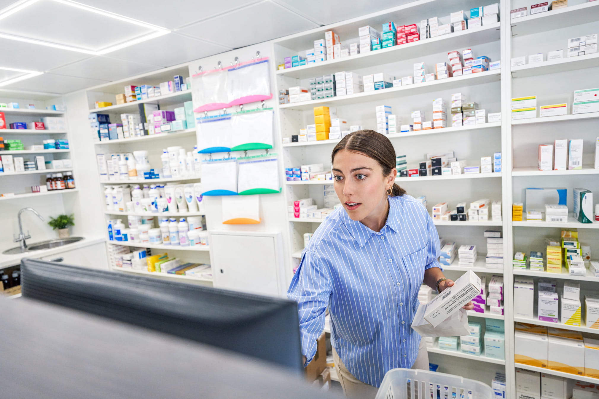 Young pharmacist behind the counter checking some information on the computer desktop