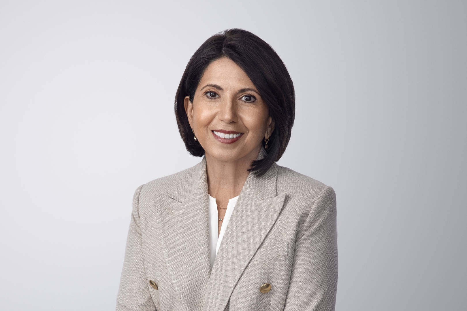 Fotografia di Silvana Battaglia. Silvana, una persona dalla pelle chiara con i capelli castani e gli occhi marroni, indossa orecchini e sorride alla telecamera. Indossa una giacca blazer grigia sopra una camicia bianca e una collana. Si trova di fronte a uno sfondo grigio chiaro senza alcun ambiente.